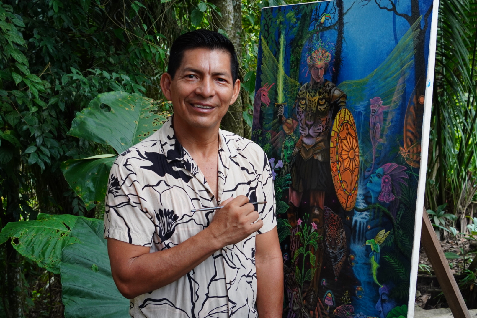 Moisés Llerena with brush in hand beside a visionary jaguar painting in the Amazon